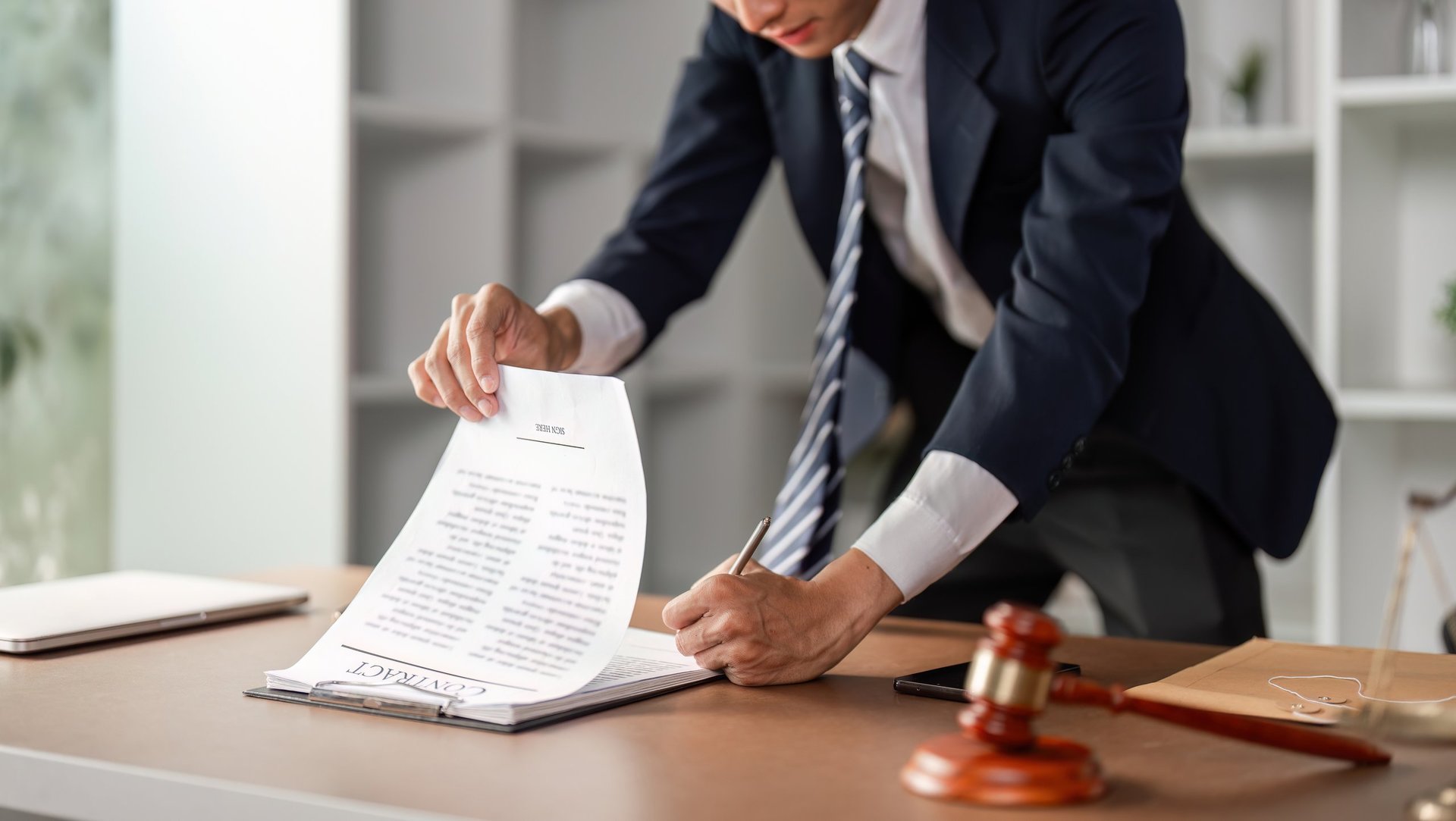 A young lawyer reviewing and signing legal contract documents at his office desk