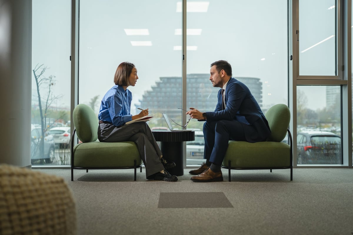 Two diverse professionals in a modern office engaged in a serious meeting, one speaking while the other listens
