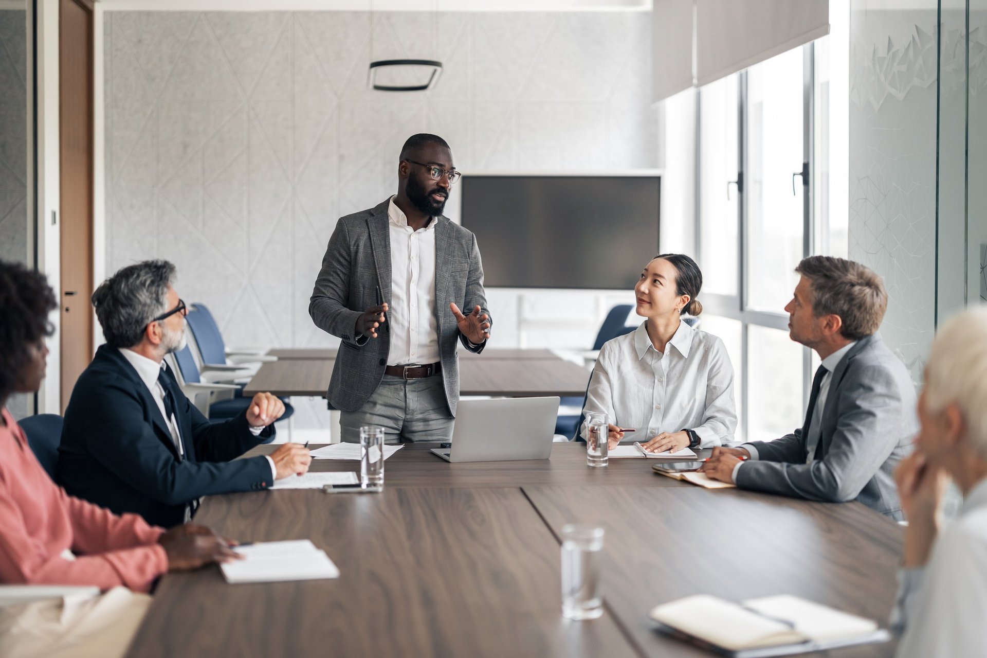 Executive presenting acquisition strategy to diverse team in modern boardroom